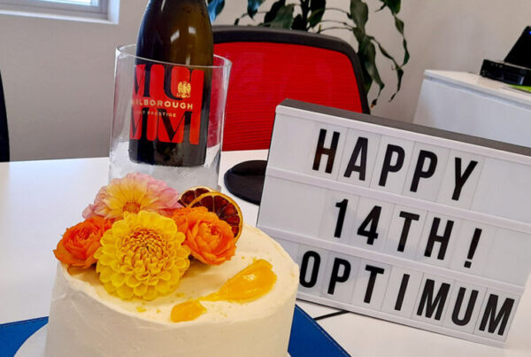 A cake, a champagne bottle on ice, and a sign saying "Happy 14th Optimum" to celebrate the 14th birthday of Optimum Recoveries.